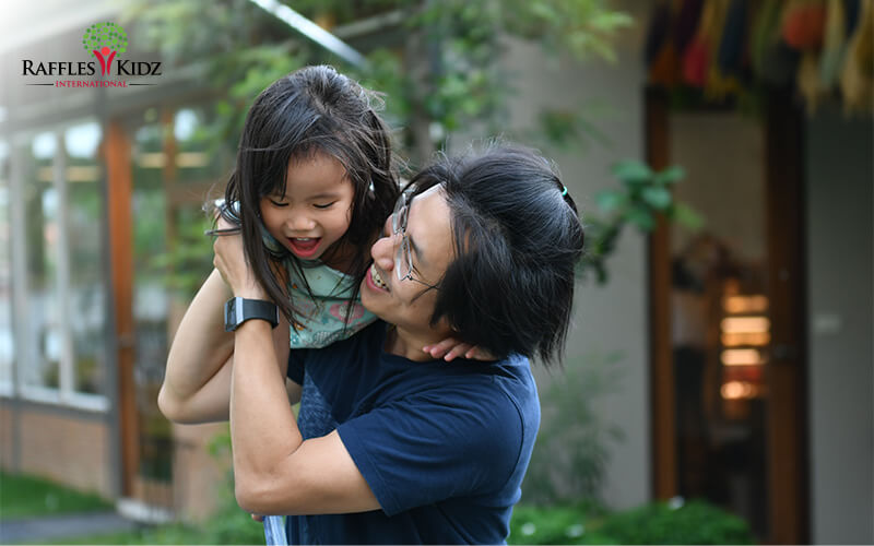 Adult holds smiling child outside building with decorations.