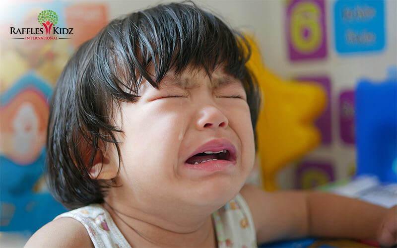 Young child crying in colorful daycare classroom.