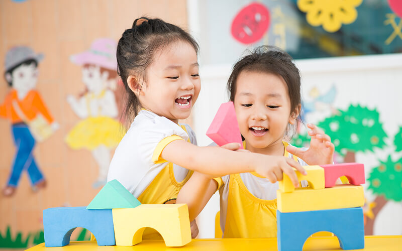 Two happy children playing with colorful building blocks together.