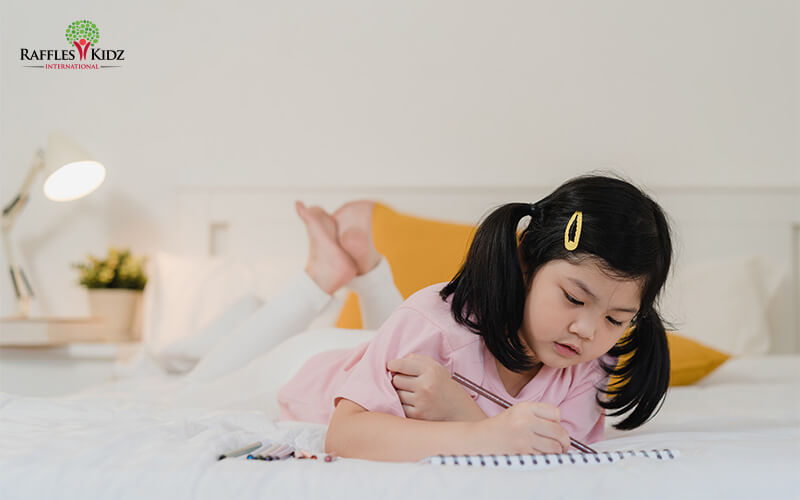 Young Raffles Kidz student drawing and writing in her notebook.