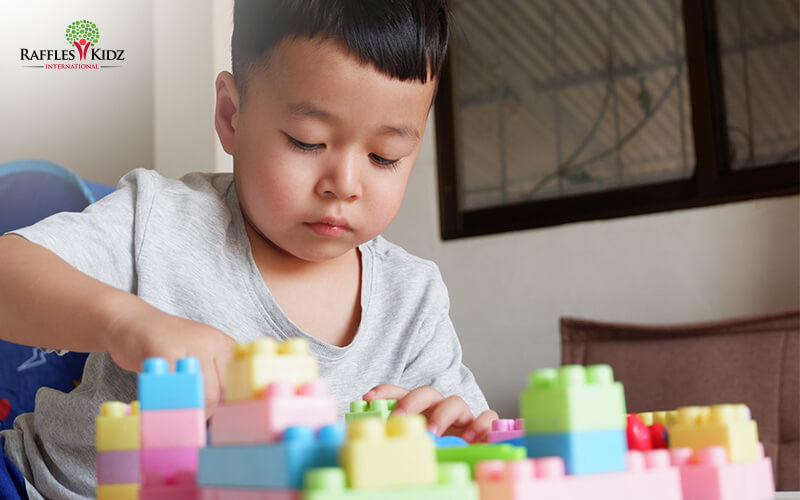 Boy focused on building block structure to meet preschool milestones.
