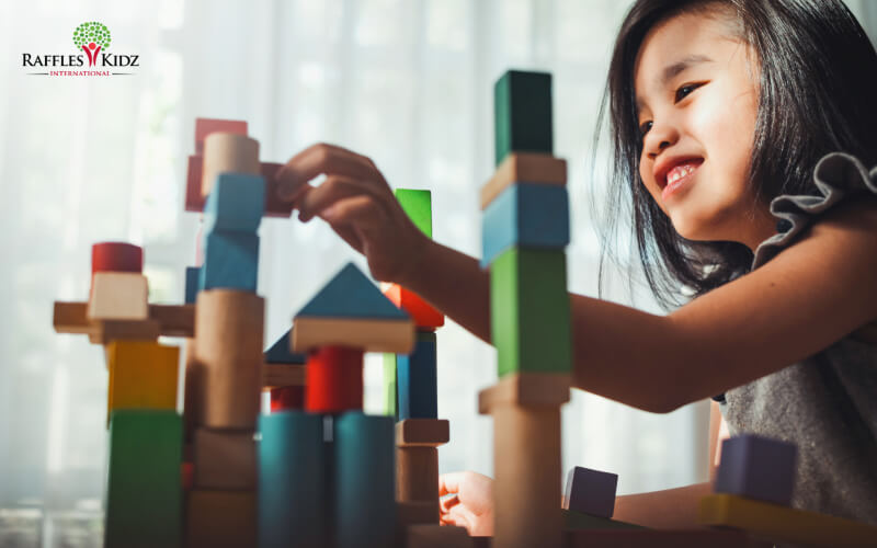 Happy girl building a tall structure with colored blocks.